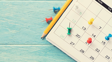 A calendar with push pins and a pencil.